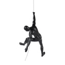 A matte black sculpture of a man climbing, mounted on a wall with a stainless steel wire.